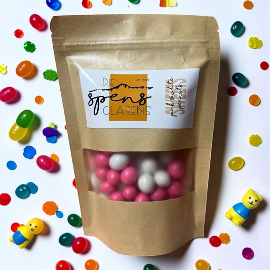 Die Spens Clarens pink and white candy-coated peanuts in a resealable brown pouch, surrounded by colorful candies and small toys.
