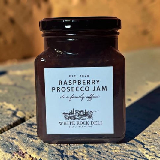 Die Spens Clarens White Rock Deli Raspberry Prosecco Jam in a glass jar with a black lid. The jam is dark red and appears to have fruit pieces.
