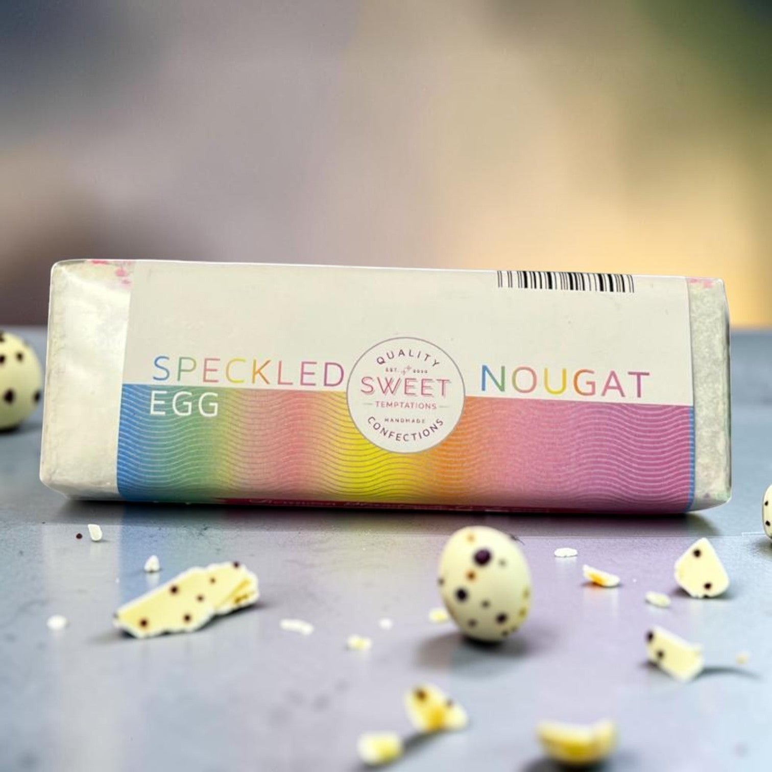 Die Spens Clarens speckled egg nougat bar with a white chocolate shell speckled with dark chocolate, surrounding small speckled eggs and broken pieces.