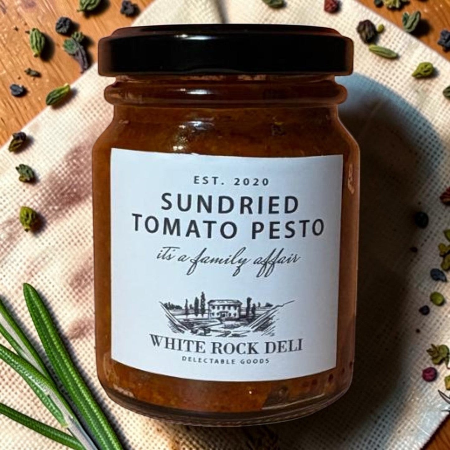 Die Spens Clarens Sundried Tomato Pesto in a glass jar with a black lid, featuring a white label with product details and a scenic illustration.