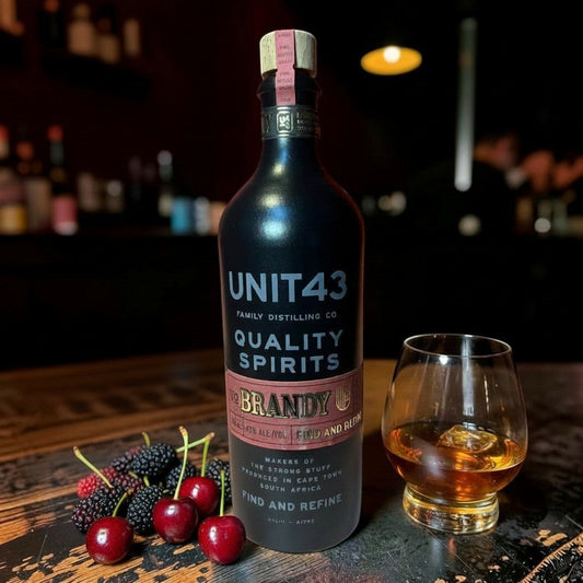 Die Spens Clarens Unit 43 Brandy in a matte black bottle, served with cherries and mulberries, alongside a glass of brandy.