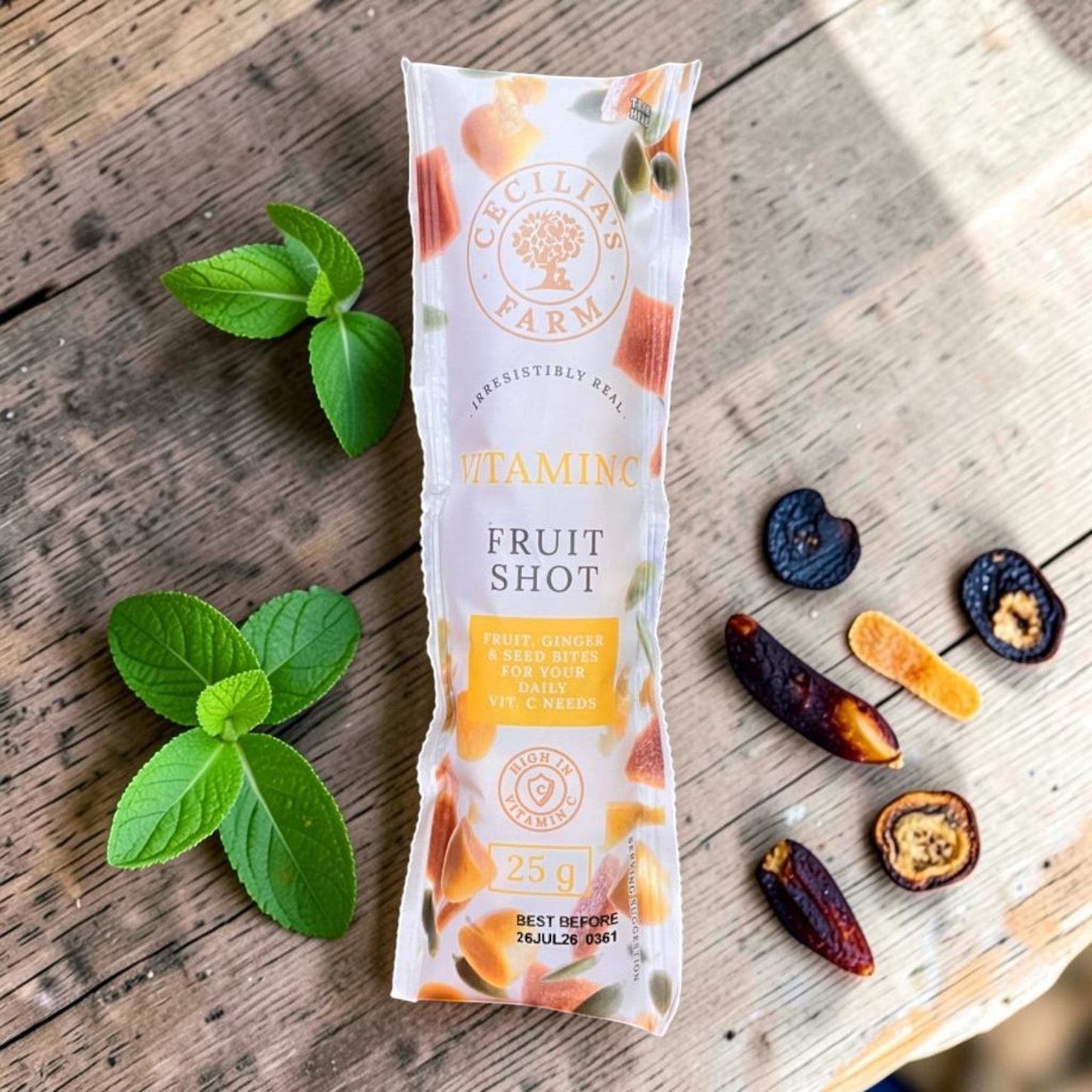 Die Spens Clarens Vitamin C Fruit Shot, a single-serving packet with fruit, ginger, and seed bites for daily Vitamin C needs. Includes mint leaves and dried fruit pieces.