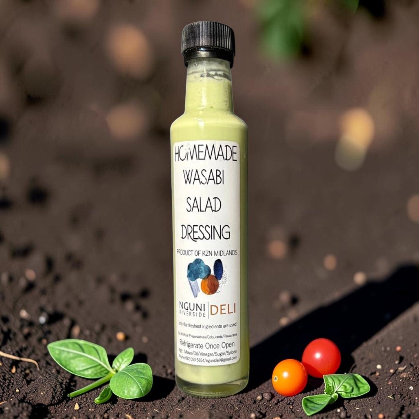 Die Spens Clarens homemade wasabi salad dressing in a glass bottle, creamy green colour, with basil and cherry tomatoes.