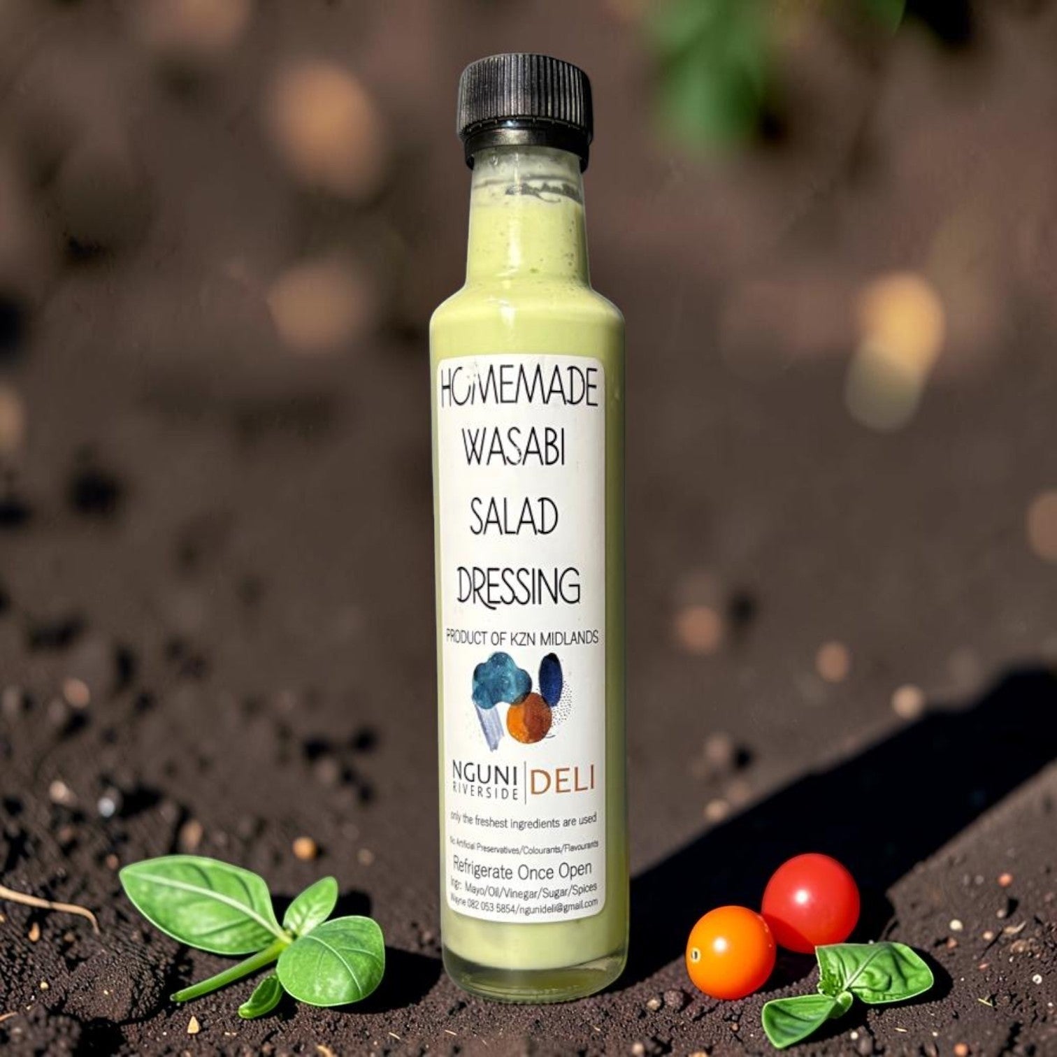 Die Spens Clarens homemade wasabi salad dressing in a glass bottle, creamy green colour, with basil and cherry tomatoes.
