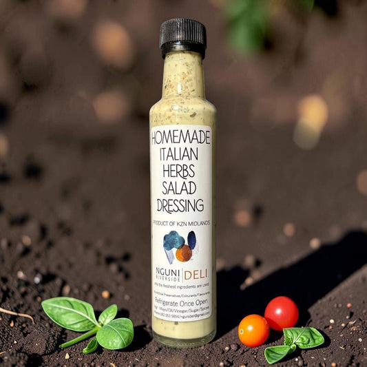 Die Spens Clarens Nguni Deli Italian Herbs Salad Dressing in a glass bottle with a black cap, surrounded by fresh basil and cherry tomatoes on dark soil.
