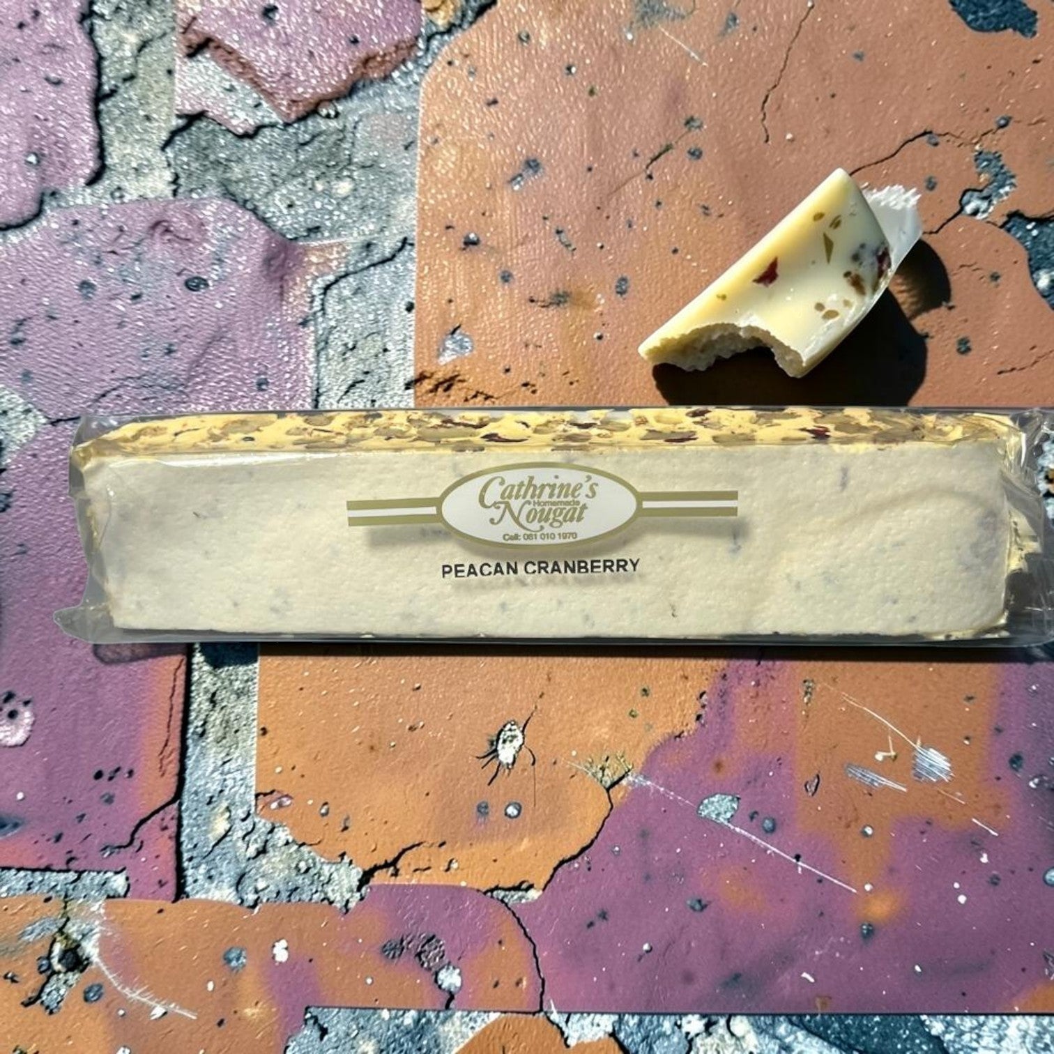 Die Spens Clarens homemade pecan cranberry nougat bar with a piece broken off, showing chewy texture with nuts and dried fruit.