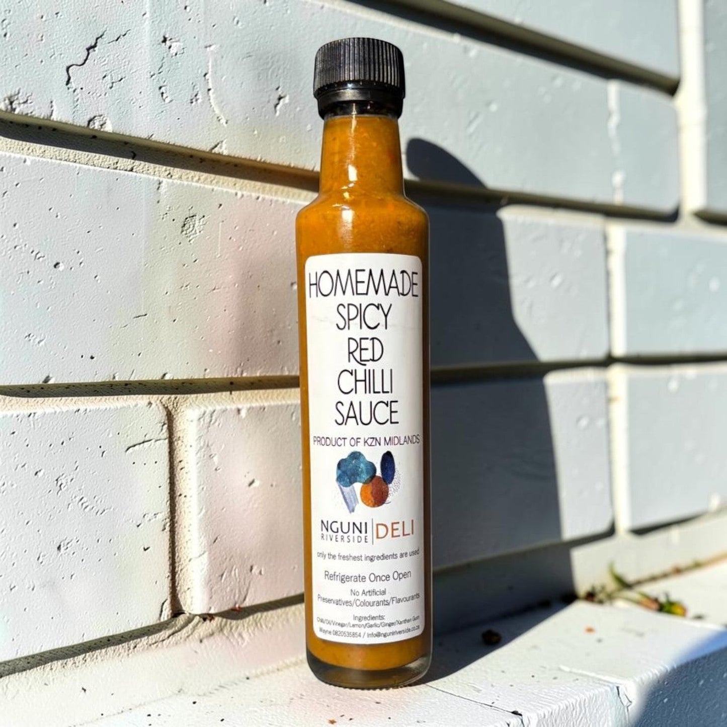 Die Spens Clarens homemade spicy red chilli sauce in a glass bottle with a black cap. Vibrant orange sauce with visible chilli flakes.