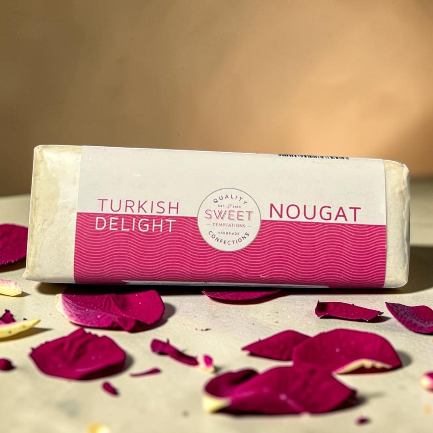 Die Spens Clarens handmade Turkish Delight Nougat bar with pink wavy pattern packaging, surrounded by rose petals.