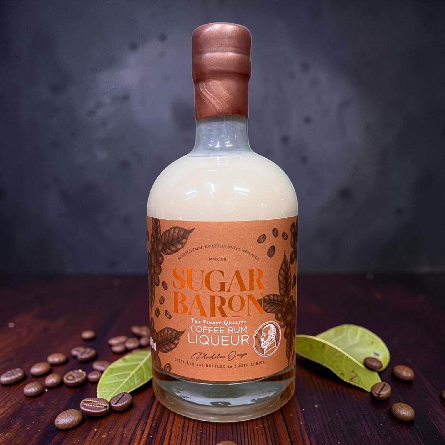 Die Spens Clarens Sugar Baron Coffee Rum Liqueur bottle with creamy beige liquid and copper cap, surrounded by coffee beans.